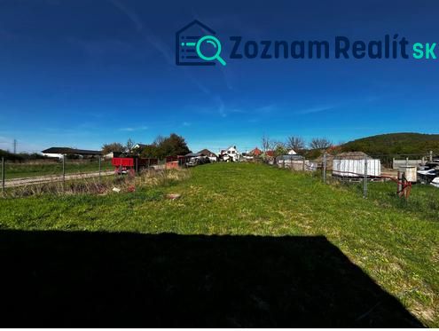 Pozemok v obci Pernek  - Pozemky - bývanie v Perneku, otvorená zelená plocha, s oplotením a vidieckou scénou v pozadí.