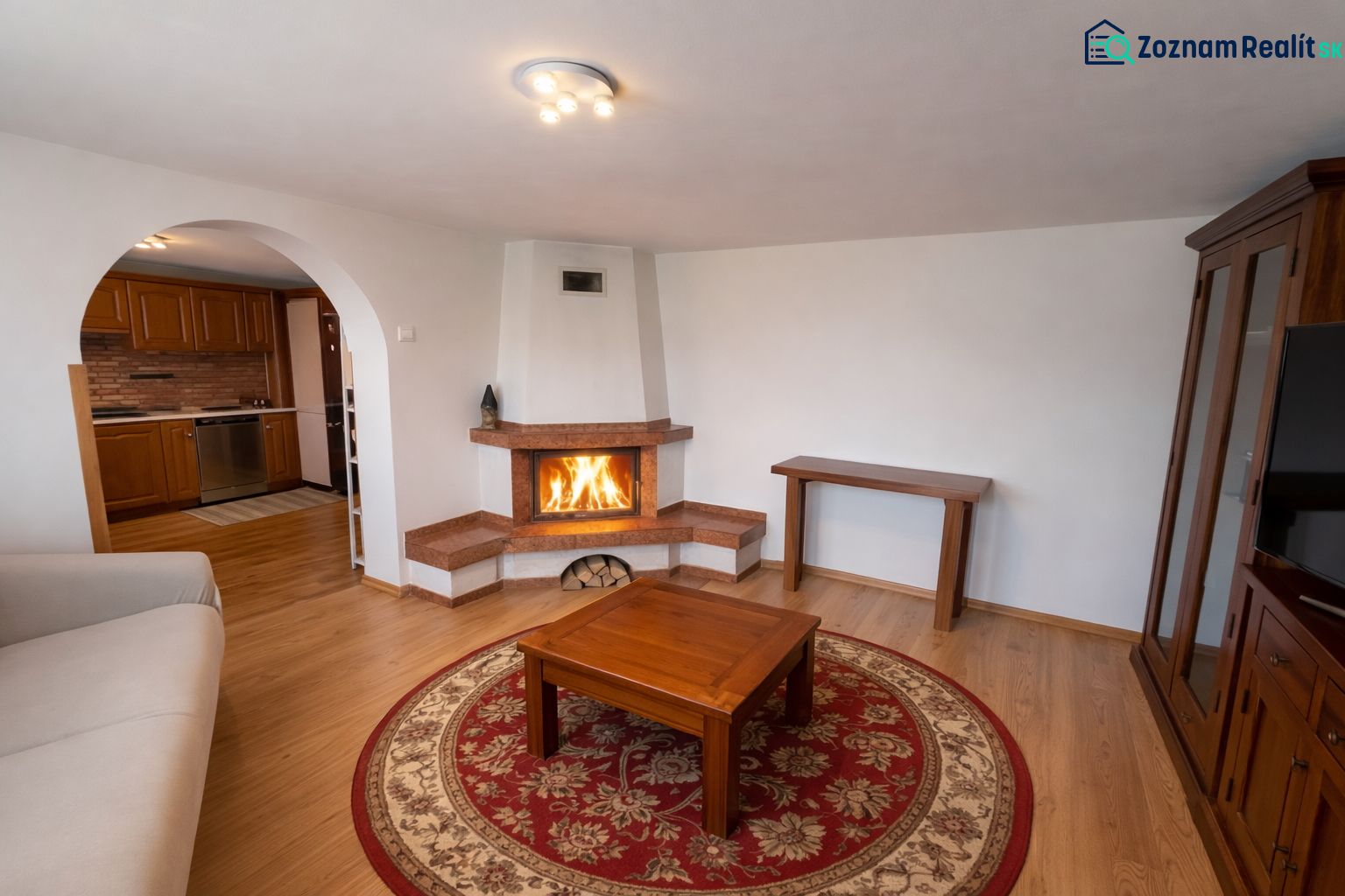 Rodinný dom Bacúch – rekonštrukcia. - Obývačka v rodinnom dome s krbom, podlahou s dreveným dekorom a oblúkovým prechodom.