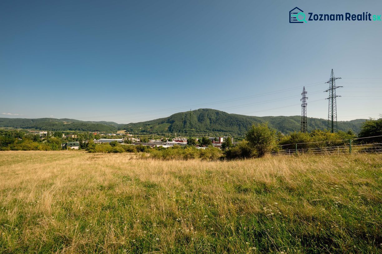 Na predaj stavebný pozemok pre rodinné domy – Banská Bystrica P306ZL - Krajina s trávnatým pozemkom a elektrickými stĺpmi na Partizánskej ceste, Banská Bystrica. Pozemky - bývanie.