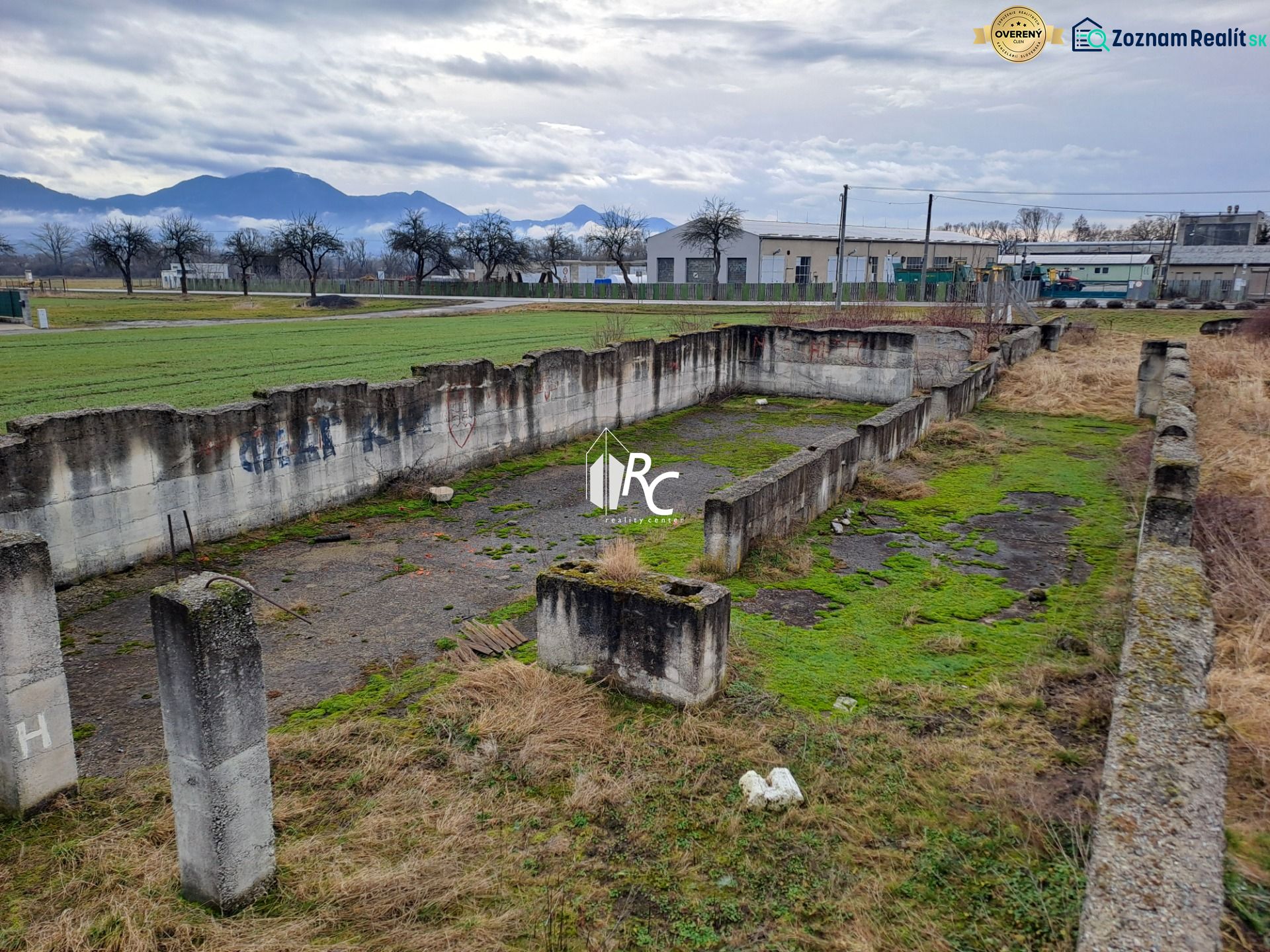 Stavebný pozemok 2 335 m² v obci Valča  - Opustené betónové základy na pozemkoch na bývanie v obci Valča s výhľadom na kopce.
