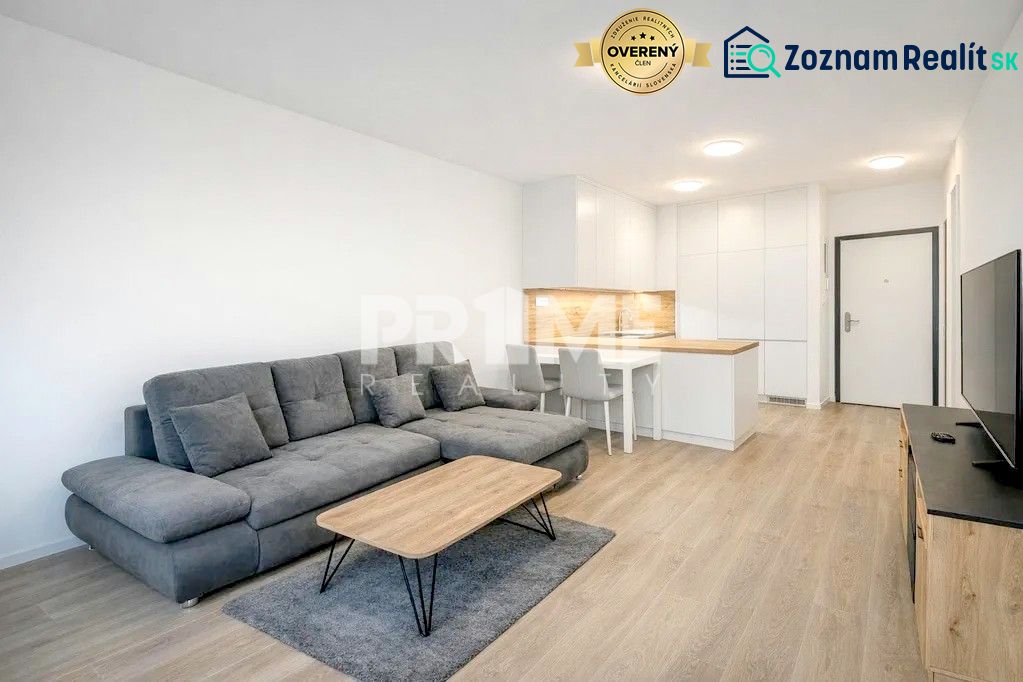 U NÁS !!! MODERNÝ 2i,NOVOSTAVBA, LOGGIA, Slnečnice UNIQ, Fialova ulica - Obývacia izba v 2-izbovom byte, sivá sedačka, televízia a podlaha s dreveným dekorom.