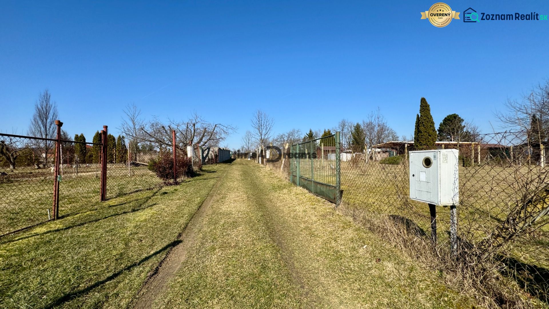 NA PREDAJ Pozemok Párovské Háje - Cesta obklopená plotmi a trávou, v záhradách Párovských Hájov.