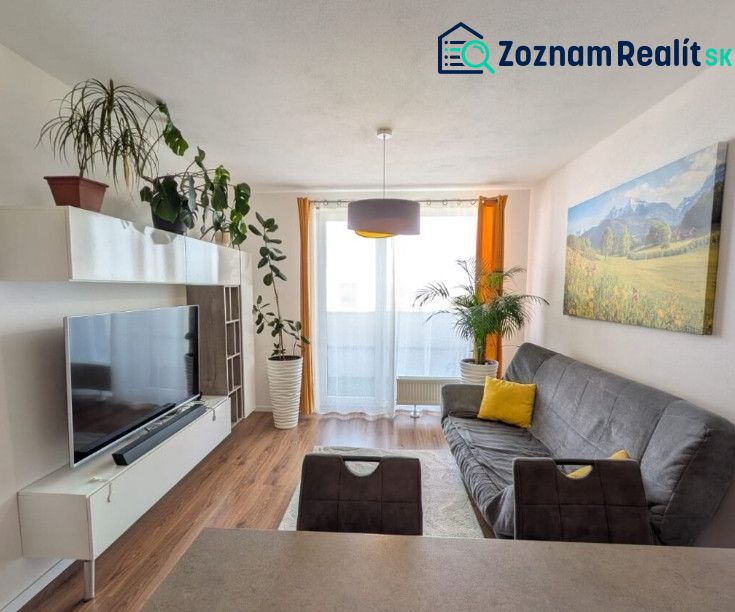 Moderný 2-izbový byt s balkónom a výhľadom - Svetlá obývačka s rastlinami, pohovkou a podlahou s dreveným dekorom v 2-izbovom byte.