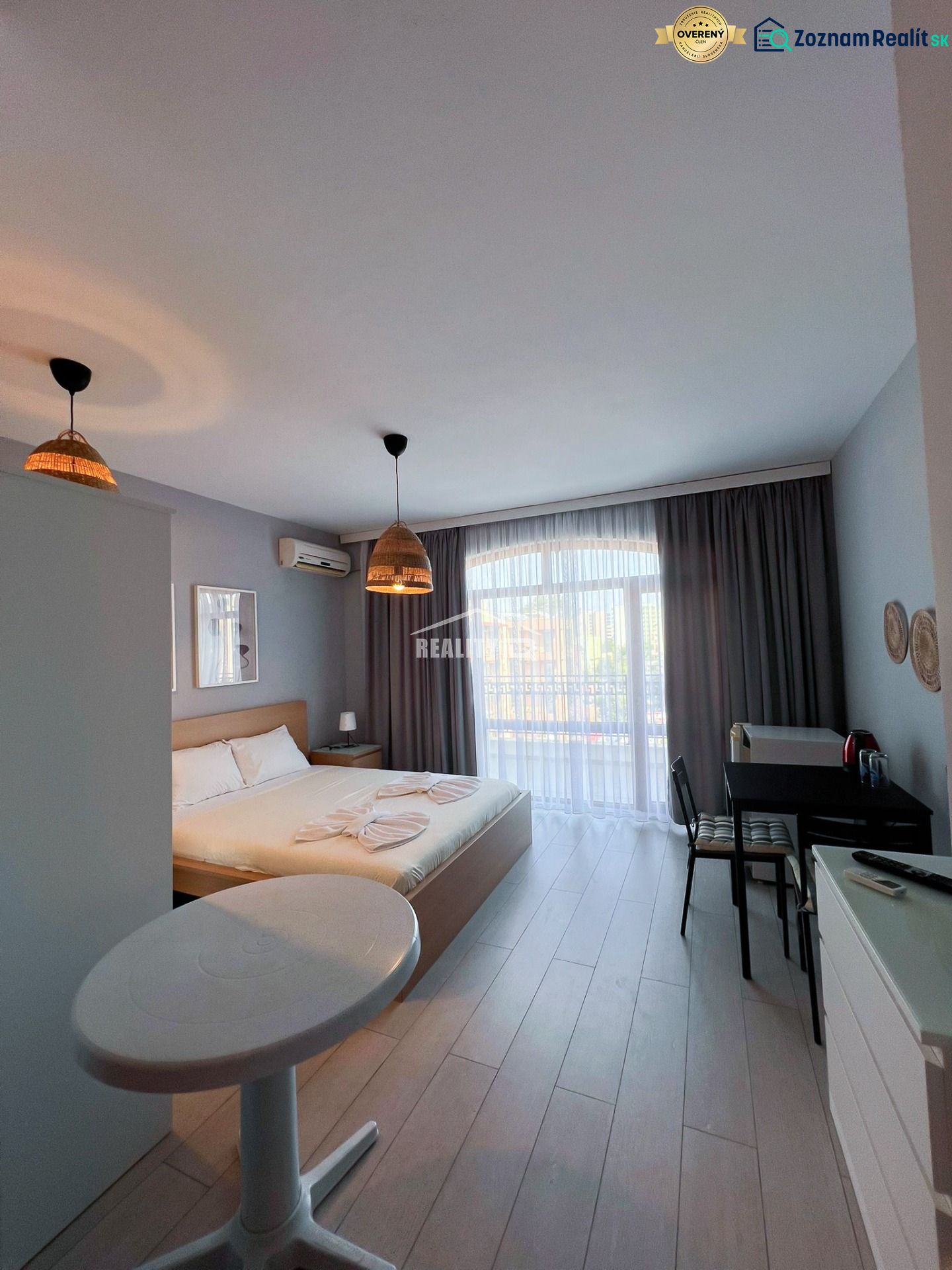 Moderná garsónka (41 m²) s výhľadom na bazén – Rezort ANTARES - Garsónka s manželskou posteľou, stolom a stoličkami, podlaha s dreveným dekorom.