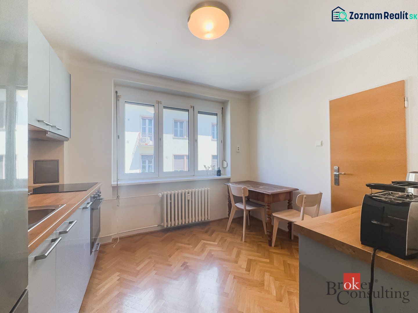 Staromestský 2i byt s balkónom na Palisádach - Kuchyňa v 2-izbovom byte s podlahou s dreveným dekorom a dreveným stolom.