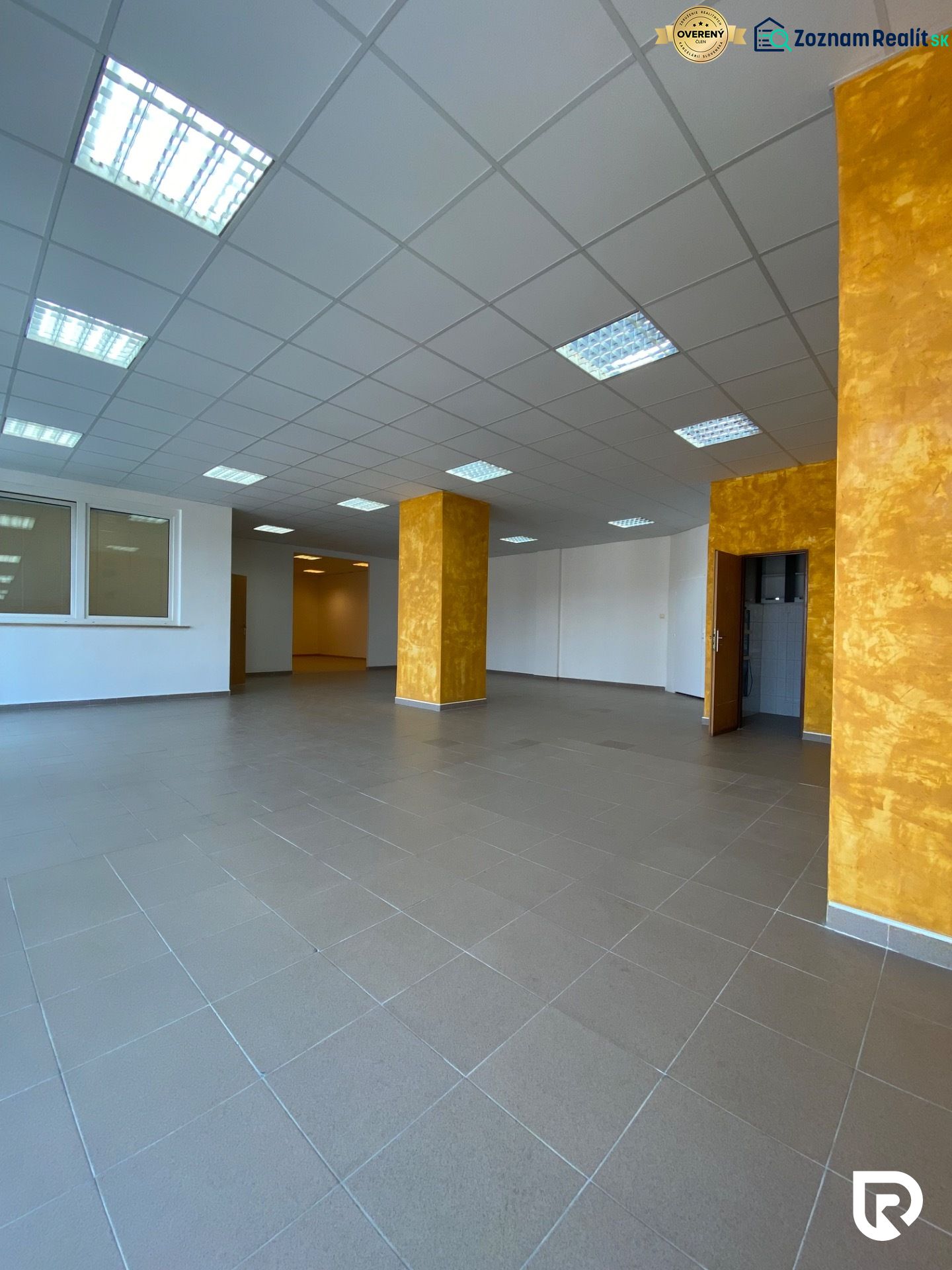 Prenájom 148,25 m² showroom, predajňa | Zlatovce - Interiér obchodných priestorov s dlažbou a oranžovými stĺpmi.