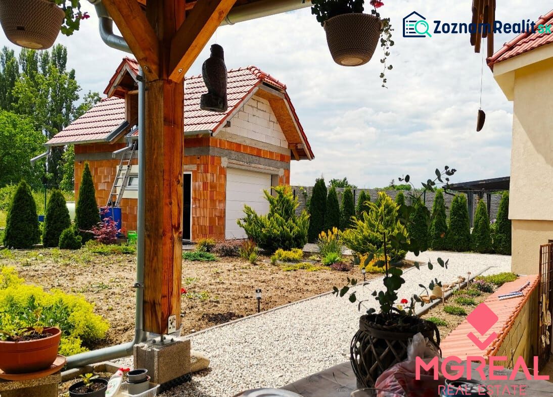 6 - izbový rodinný dom v obci Ratkovce, novostavba - Upravená záhrada a garáž pri rodinnom dome v Ratkovciach, obklopené zeleňou a drevom.