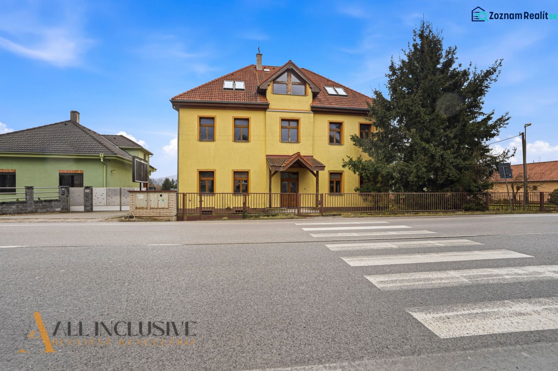  POLYFUNKČNÝ OBJEKT | CHRABRANY | TOPOĽČANY - Budova s krémovou fasádou na ulici Chrabrany v Topoľčanoch. Vedľa rastie veľký ihličnan.
