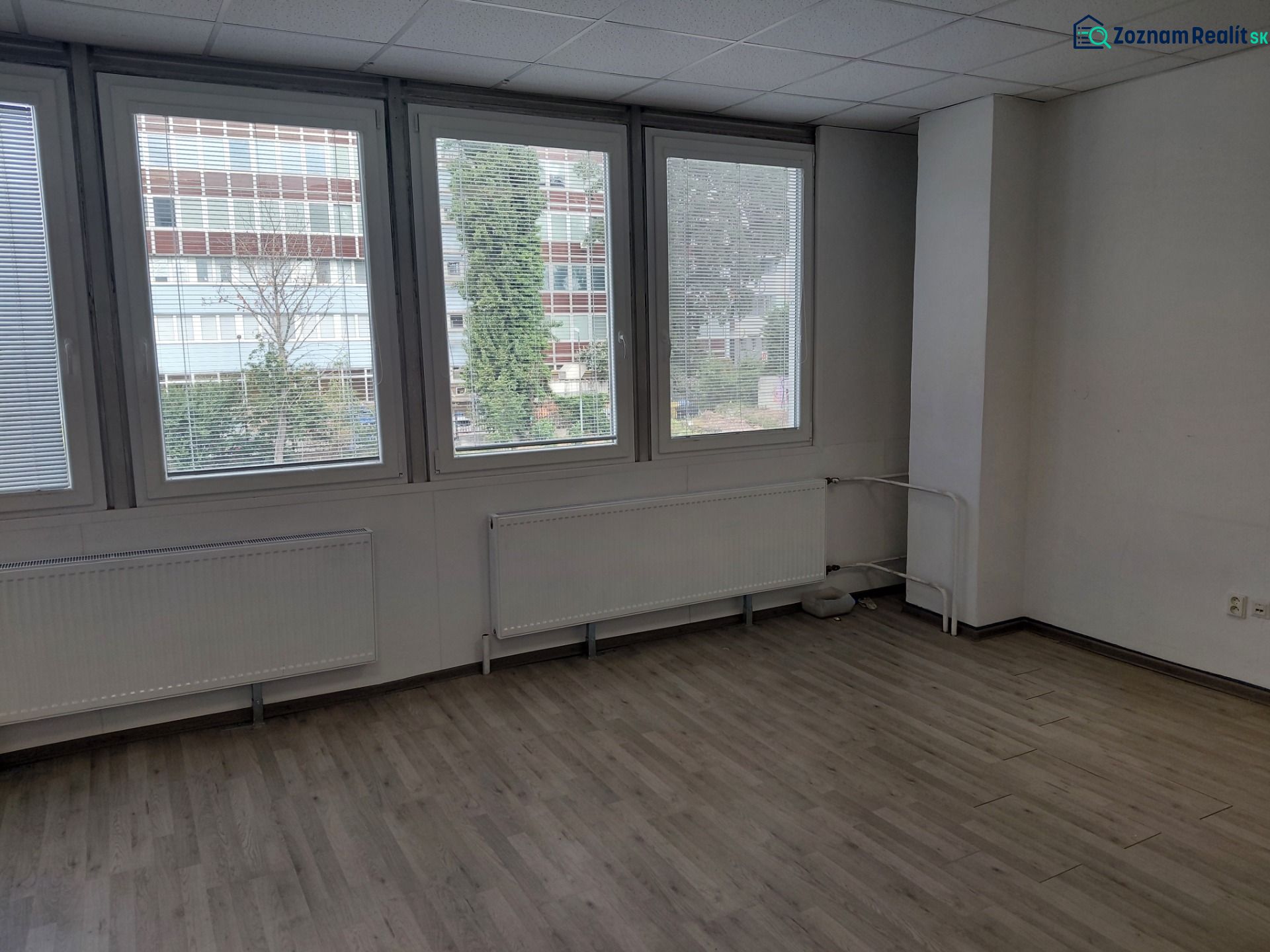 Klimatizovaná kancelária 39 m2 s umývadlom na Tomášikovej ul.  - Kancelárie s veľkými oknami, neutrálne steny, podlaha s dreveným dekorom.