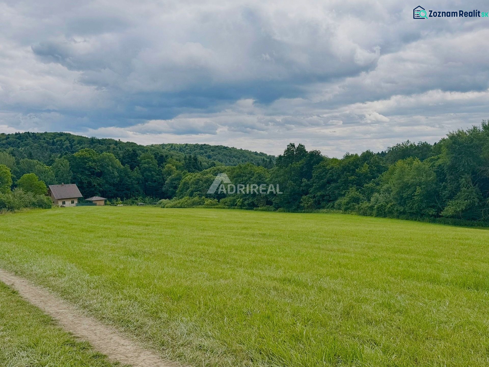 PREDAJ: rekreačný pozemok 564 m2;Bardejov-Zlaté; 39.900 € - Zelené Rekreačné pozemky v Bardejove s lesom a domom v pozadí.