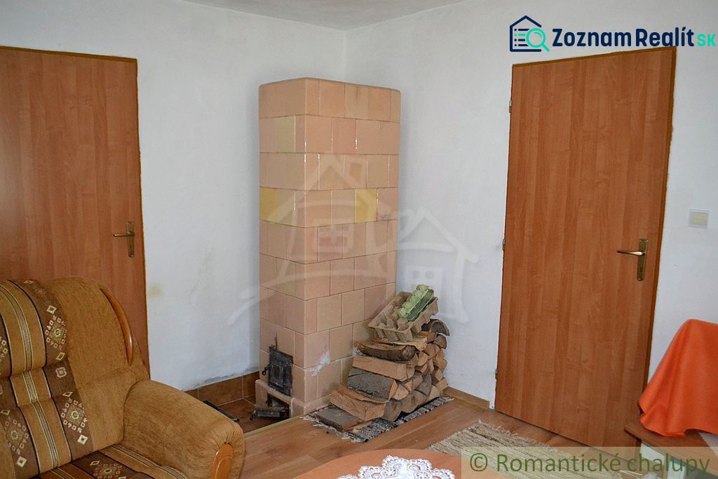 Dom so zrekonštruovaným interiérom - Varadka - Izba v rodinnom dome s kachľovou pecou a podlahou s dreveným dekorom.