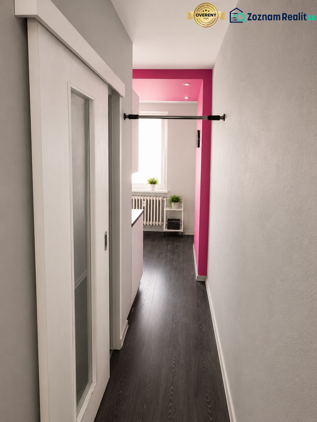 REZERVOVANÝ - Na predaj priestranný 2-izbový byt s balkónom, klímou... - Chodba 2-izbového bytu s posuvnými dverami, podlaha s dreveným dekorom, ružová stena.