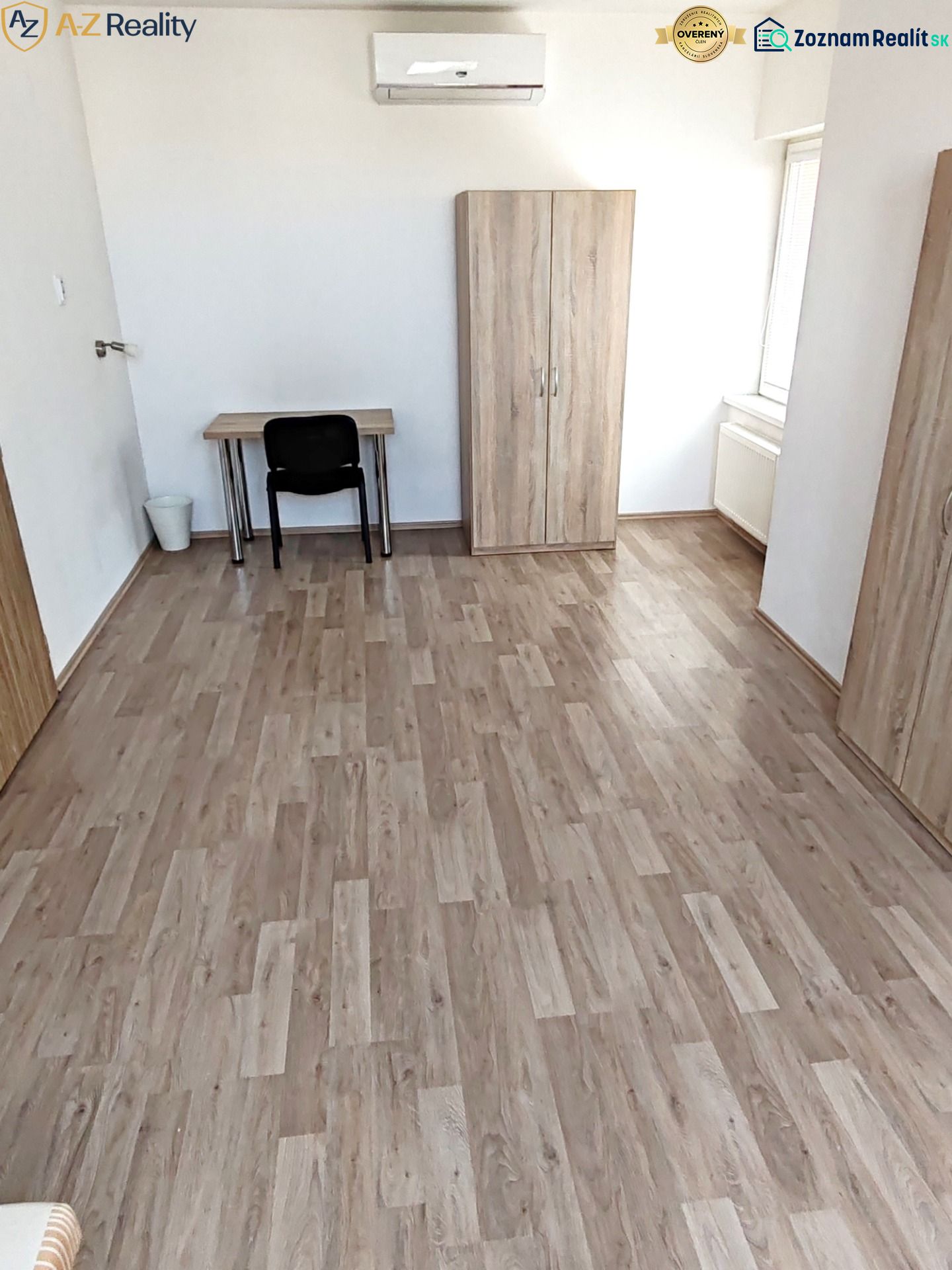 Väčší 1 izbový byt na prenájom v Komárne - Izba v 1-izbovom byte s podlahou s dreveným dekorom, stolom a skriňou.