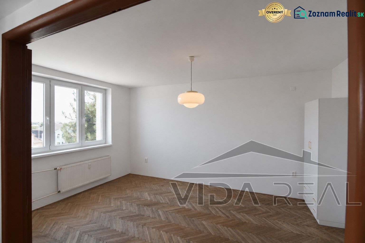 Priestranný 3-izbový byt | 72 m² + 9 m² loggia + 9 m² pivnica |  - Obývacia izba v 3-izbovom byte s podlahou s dreveným dekorom a veľkými oknami.