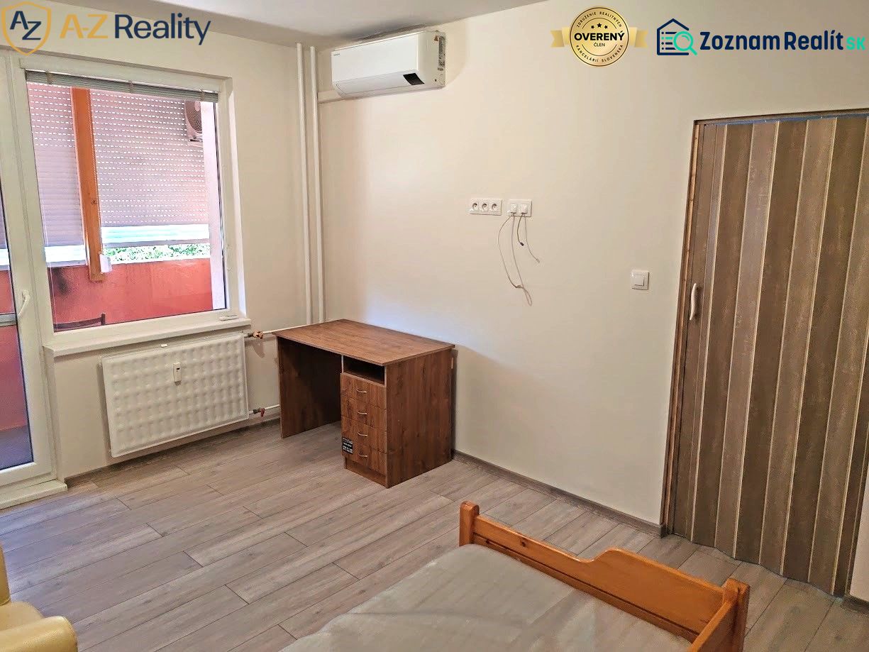 Pekný 1 izbový byt s balkónom na prenájom - 1-izbový byt s podlahou s dreveným dekorom, stolom a radiátorom pri okne.
