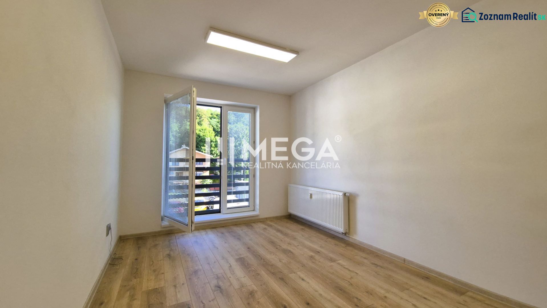 PRENÁJOM kancelárie blízko centra Humenného (15,20 m2) - Kancelária s veľkým oknom, podlahou s dreveným dekorom a radiátorom.