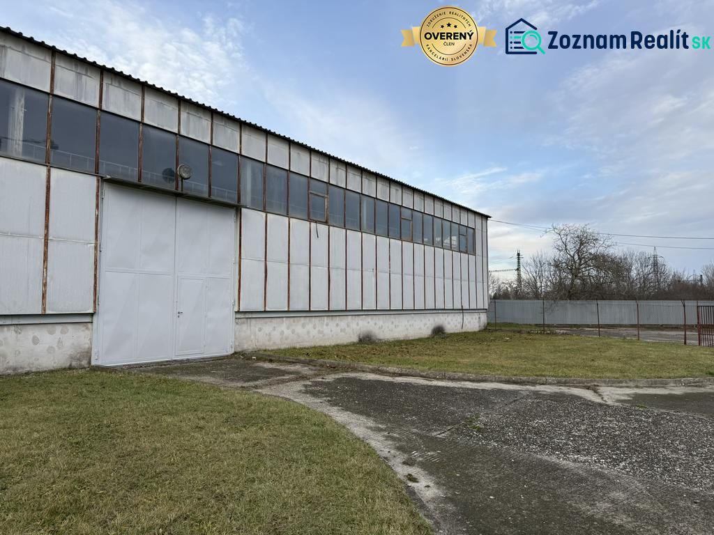 Sklad. priestory 200m2 - 1000m2, spevnené plochy do 6000m2 v areáli. - Skladová hala v Bratislave-Rači s oceľovou konštrukciou a zeleným trávnikom v popredí.
