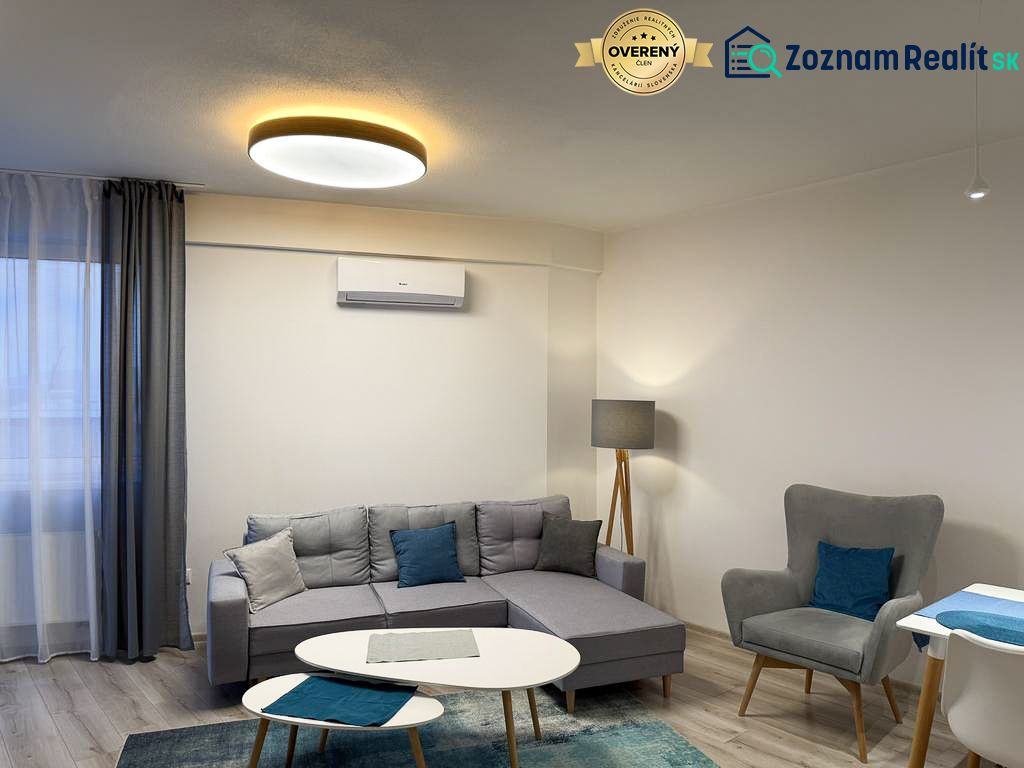 Nové skolaudované byty a apartmány vo Vajnoroch. - Obývacia izba v 2-izbovom byte s podlahou s dreveným dekorom a sivými sedačkami.