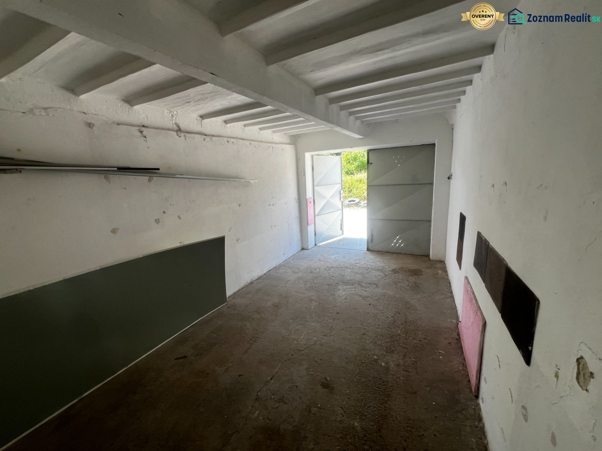 Ponúkame na predaj garáž, Vyhnianska cesta, Bratislava - Nové Mesto. - Interiér garáže s betónovou podlahou a otvorenými plechovými dverami.