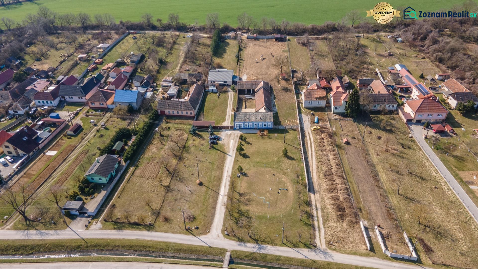 Stavebný pozemok 8 500 m² s podnikateľským potenciálom - Dedinský pohľad na pozemky v Dolnom Lopašove so záhradami a domami na bývanie.