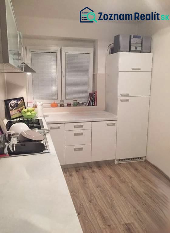 Prerobený 2 izbový byt v centre mesta Nové Zámky - Kuchyňa v 2-izbovom byte s bielymi skrinkami a podlahou s dreveným dekorom.
