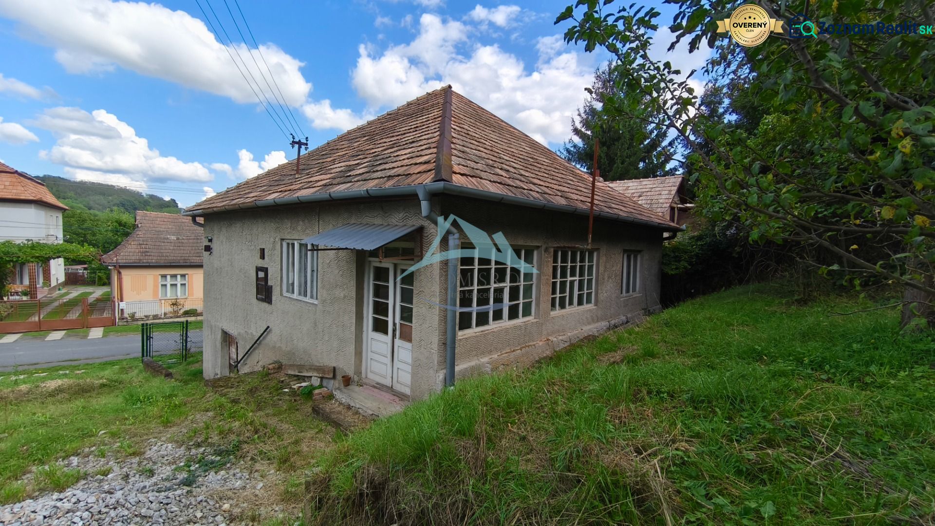 Znížená cena!!! Vidiecky dom v obci Olováry v okrese Veľký Krtíš. - Rodinný dom v Olovároch so šikmou strechou, obklopený záhradou a zelenými stromami.