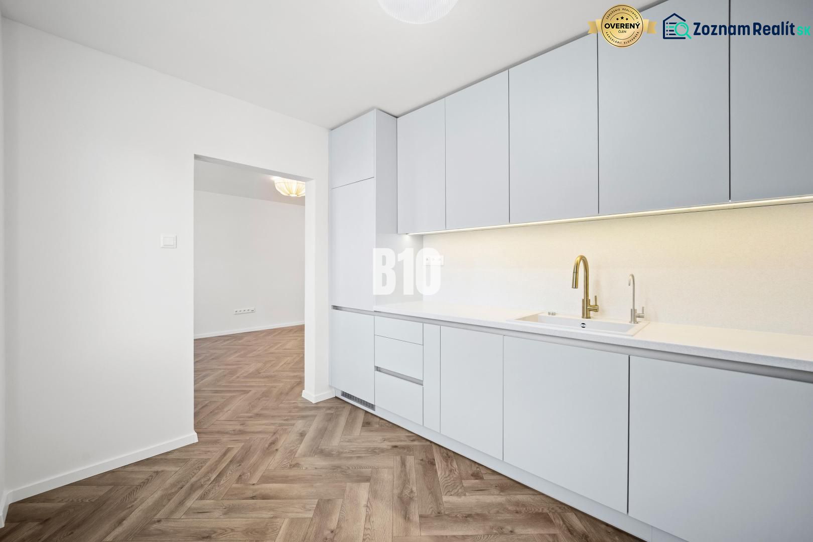 Prémiové bývanie v centre Nitry | 3 izby, veľký balkón - Kuchyňa v 3-izbovom byte s bielym nábytkom a podlahou s dreveným dekorom.