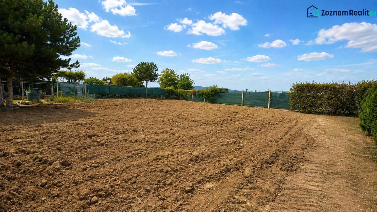 NA PREDAJ – rovinatý stavebný pozemok v Pravoticiach | 660 m² - Pozemky na bývanie v Pravoticiach s obrábanou pôdou, zeleným plotom a modrou oblohou.