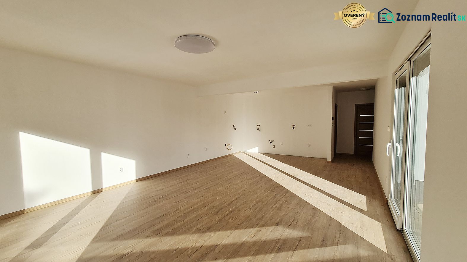 / Novostavba, moderný bungalov, dokončený na kľúč  - Interiér rodinného domu s podlahou s dreveným dekorom a veľkými oknami.