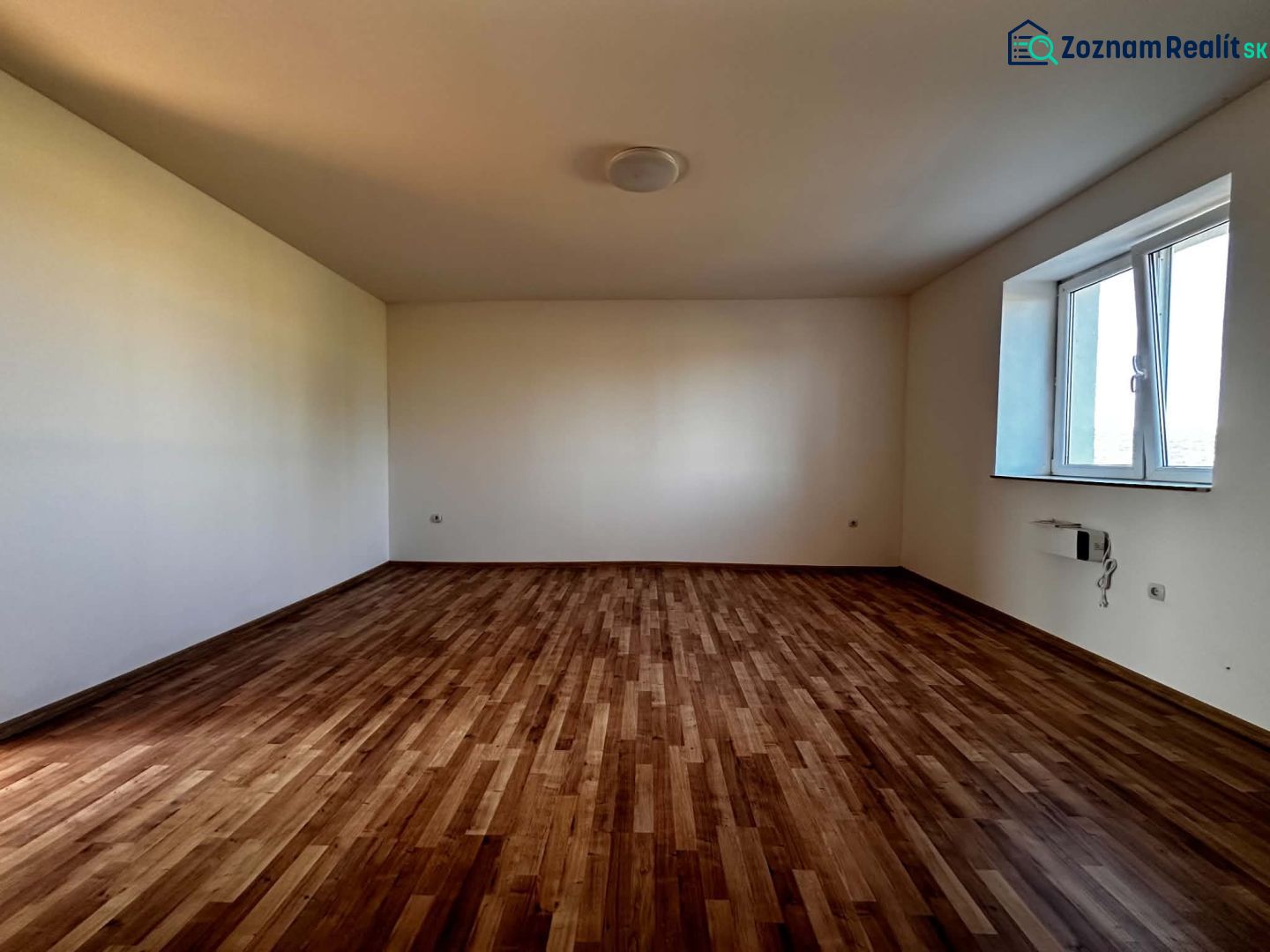 Na predaj 2-izb. byt v dvojdome (110 m²) v štandarde s krbom – Možnosť - Priestranná izba s podlahou s dreveným dekorom a veľkým oknom v rodinnom dome.