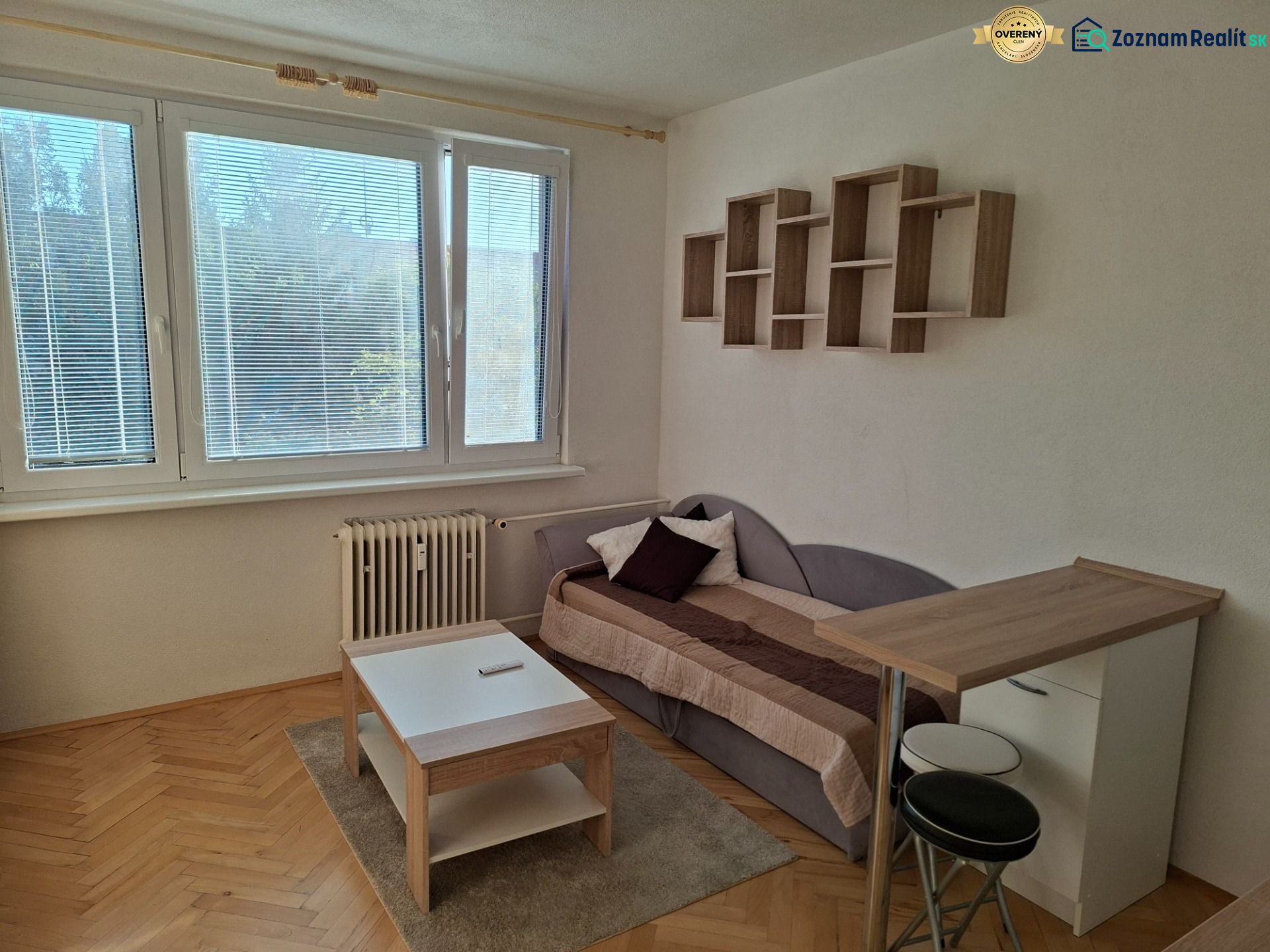 DOBRÉ REALITY-pekná garsónka na prenájom, sídl. Kopanice, Prievidza - Garsónka s podlahou s dreveným dekorom, pohovkou, stolíkom a závesnou policou.