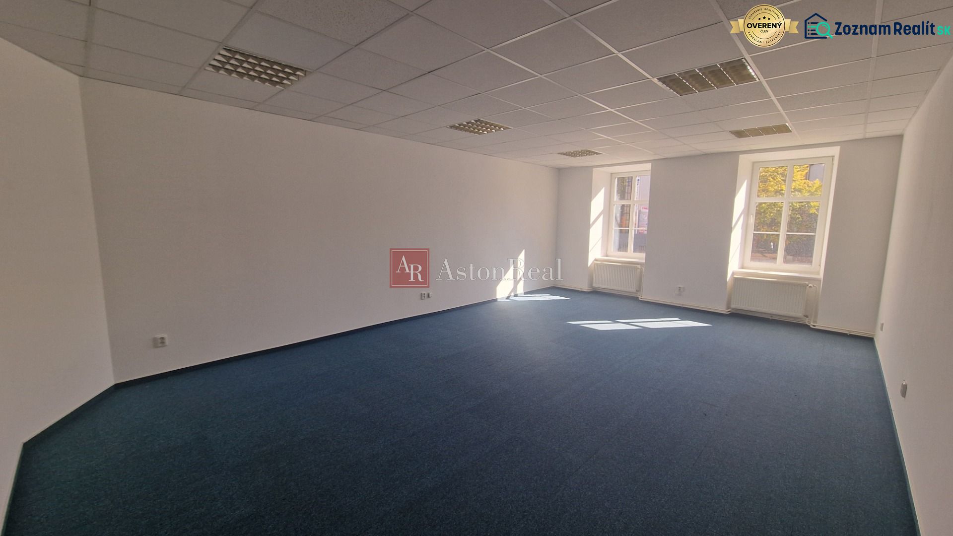 Prenájom - Poprad, kancelárske priestory centrum, 38 m2 - Svetlá priestranná kancelária s modrým kobercom a bielymi stenami.