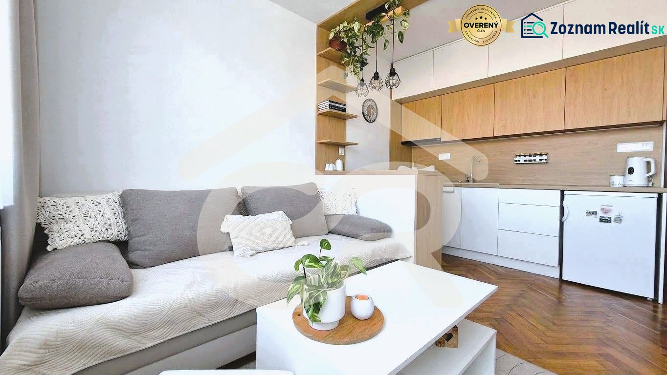 Prídeš, zamiluješ sa a bývaš - dizajnová nová garsónka na Chrenovej ! - Garsónka s kuchyňou, pohovkou, policami a podlahou s dreveným dekorom.