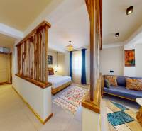 APARTMÁN NA PREDAJ V PAJE, ZANZIBAR - 1-izbový byt s drevenými doplnkami, posteľou, farebným kobercom a pohodlným sedením.