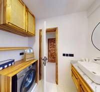 APARTMÁN NA PREDAJ V PAJE, ZANZIBAR - Kúpeľňa s umývadlom a práčkou, drevené skrinky, biela stena v 1-izbovom byte.