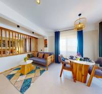 APARTMÁN NA PREDAJ V PAJE, ZANZIBAR - Obývacia časť a jedálenský kút v 1-izbovom byte s drevenými prvkami a záclonami.