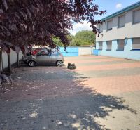 Prenájom - skladové priestory/kancelária, Vlčie hrdlo, Bratislava - Parkovisko pred modrou budovou, autá zaparkované na dlažbe, okolité stromy poskytujú tieň, kancelárie.