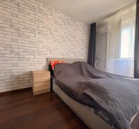 Kompletne zariadený 2-izbový byt (pôvodne 3-izb.) – Vodná ul. Komárno - 3-izbový byt na ulici Vodná: spálňa s tehlovou stenou, tmavé závesy a posteľ.