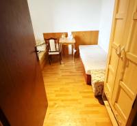 Na predaj : 3 izbový byt , centrum , Levice - Malá izba s drevenou podlahou v 3-izbovom byte, obsahuje posteľ, stôl, skriňu a stoličku.