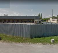 Skladový areál, Pribeník - Priestor s plechovým plotom a industriálnymi stavbami v Pribeníku, sklady a haly.