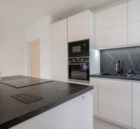 ZARIADENÝ - 3i v novostavbe 76 m2 + balkon - Trenčín - Kuchyňa v 3-izbovom byte s bielymi skrinkami, čiernou pracovnou doskou a orchideou.