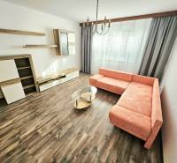 PRENÁJOM 3 IZBOVÝ BYT / 70 M2 /VEĽKOMETRÁŽNY/DUBNIČKA /LOGGIA - Obývačka 3-izbového bytu s rohovou sedačkou, závesmi a drevenou podlahou.