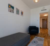 Skvelý slnečný 3i byt s balkónom v projekte METROPOLIS - Izba v 3-izbovom byte s kreslom, laminátovou podlahou a nástennými obrazy.