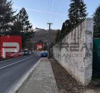 Novostavba rodinného domu v Malých Karpatoch - Cesta s chodníkom vedúcim cez Pezinok pri rodinnom dome, v pozadí kopcovitá krajina.