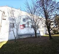 EXKLUZÍVNA INVESTÍCIA: MULTIFUNKČNÁ BUDOVA NA PREDAJ, TRNAVA - Budova so zeleňou a stromami na ulici Ľ. Podjavorinskej, v pozadí modrá obloha.