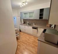 Predaj zariadený 2 izbový byt, Záhradnícka ulica,Bratislava II Ružinov - Kuchyňa v 2-izbovom byte s drevenou podlahou, bielym nábytkom a spotrebičmi.