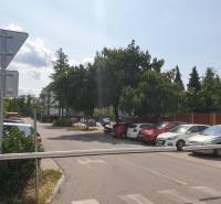 Nový priestranný 3iz. byt s klimatizáciou, balkónom a parkovaním. - Parkovisko na ulici Za dráhou, blízko Garáže, bariéra a stromy na pozadí.