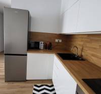 Nový priestranný 3iz. byt s klimatizáciou, balkónom a parkovaním. - Kuchyňa v 3-izbovom byte s bielymi skrinkami, drevenou pracovnou doskou a čierno-bielym kobercom.