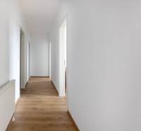 PRENAJOM | 3 Izbový byt + Loggia + Parking. PROMENADA LIVING PARK - Chodba v 3-izbovom byte s bielymi stenami a drevenou podlahou.