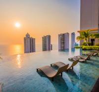 THE RIVIERA WONGAMAT BEACH PATTAYA - Bazén, ležadlá a panoráma výstavby bytov v Pattaye pri západe slnka.